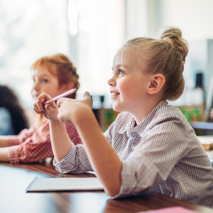Young girls smiling at their desk, listening attentively in a classroom.