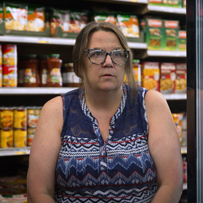 Woman sitting between store shelves and freezer display