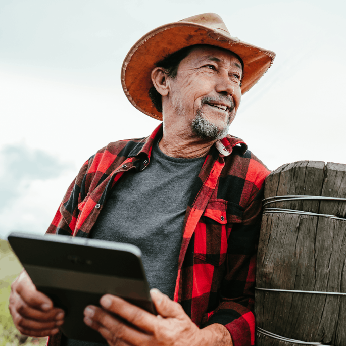 Cowboy using tablet while leaning on fence post